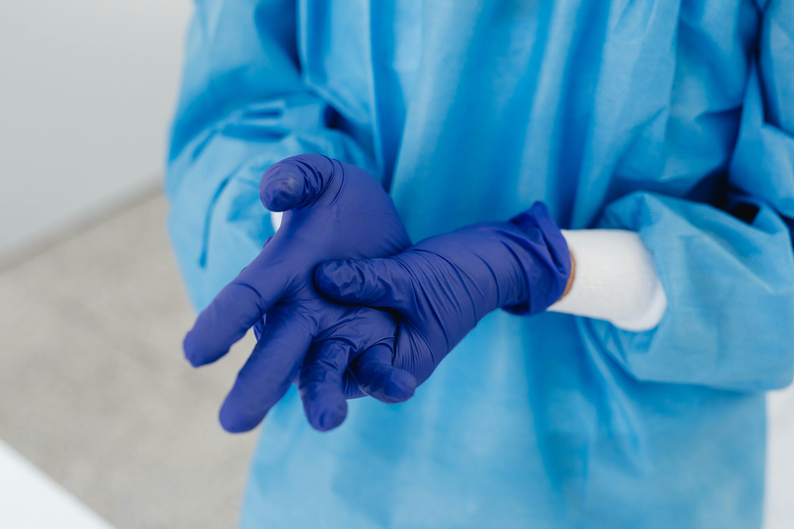 Close-up of healthcare worker wearing blue protective suit and gloves.